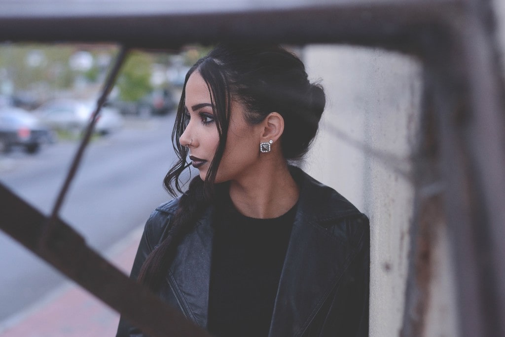 A woman wearing black stud earrings and a nose ring while standing on a sidewalk.