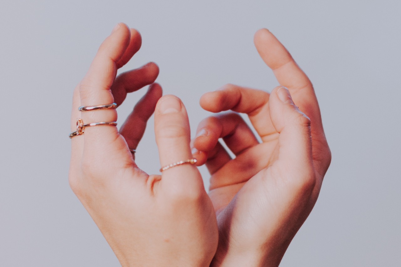 a pair of hands reaching upwards and wearing a number of thin gold rings