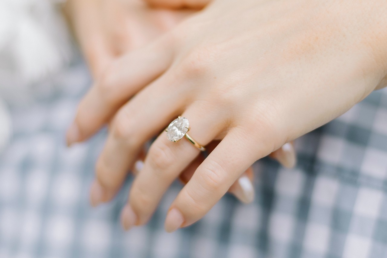 a woman’s hands, one on to pof the other, donning a yellow gold, oval cut engagement ring