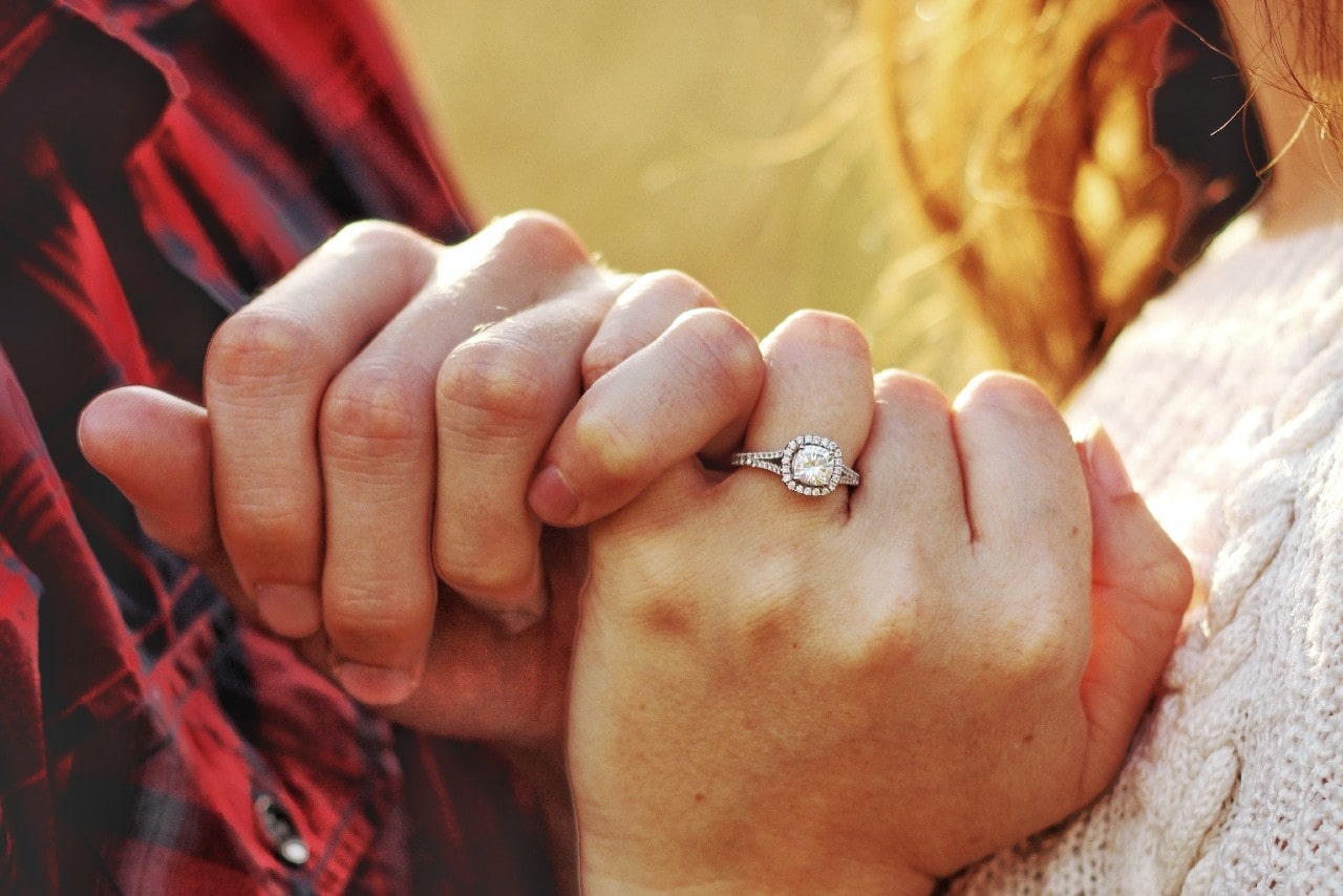 a couple crossing their pinkies, the woman wearing a cushion cut, halo engagement ring