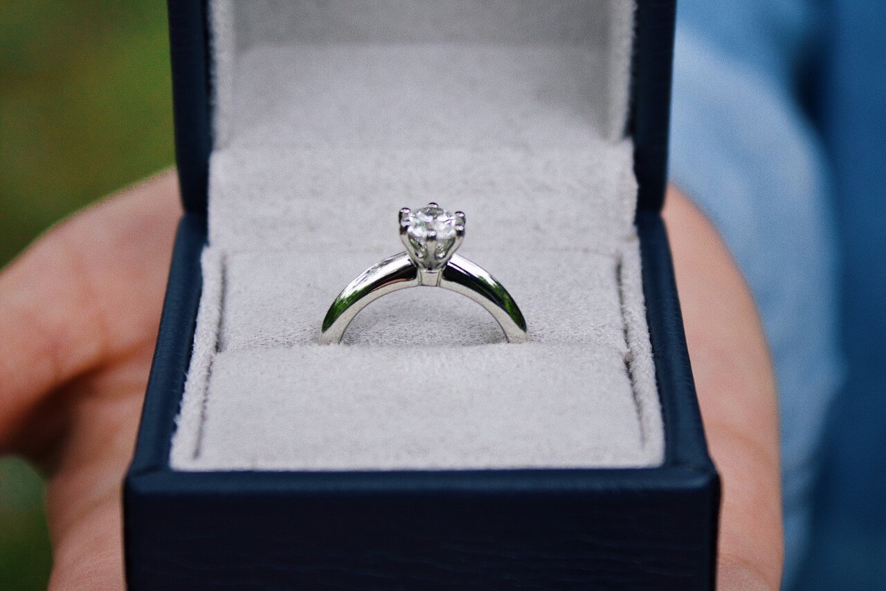 A man proposes with a platinum solitaire engagement ring in a navy blue ring box