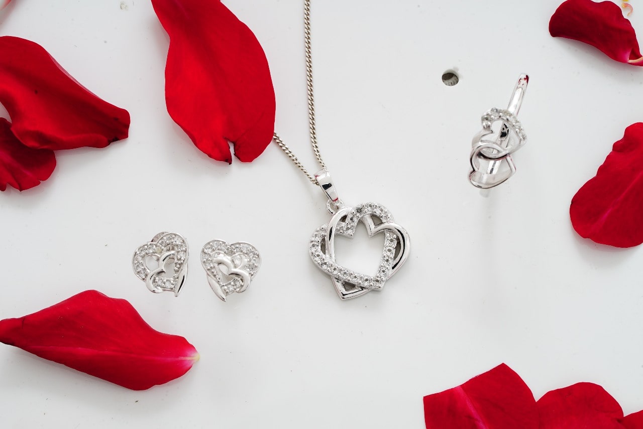 A white gold heart and diamond jewelry set on a white background with scattered rose petals