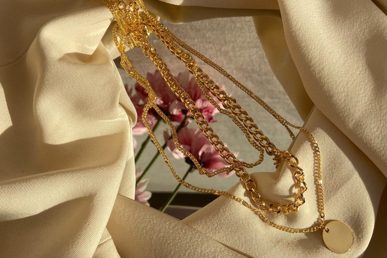Three gold necklaces lying on a mirror with a cream cloth surrounding it