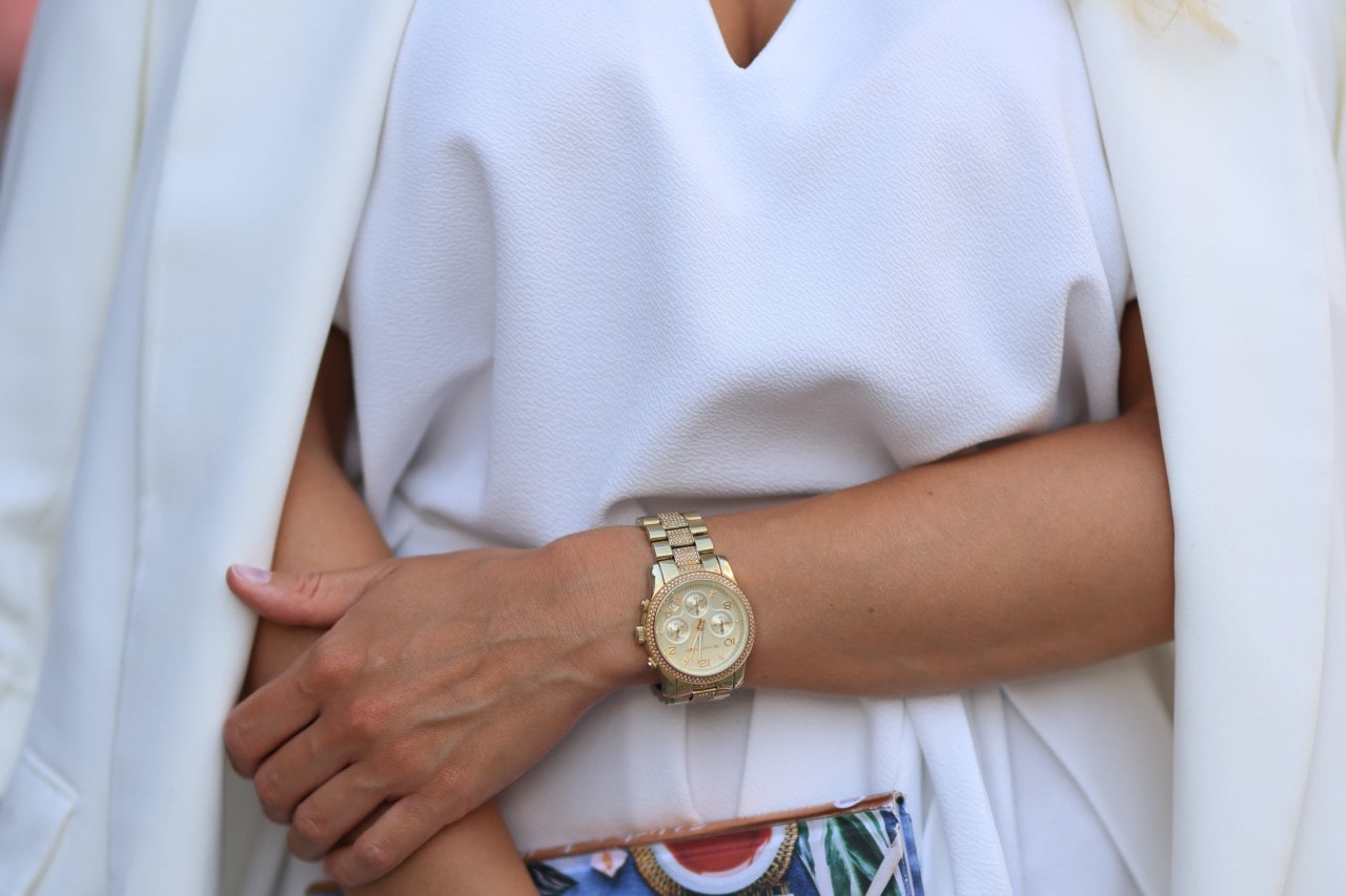 A woman wearing all white and a gold watch carrying a colorful bag