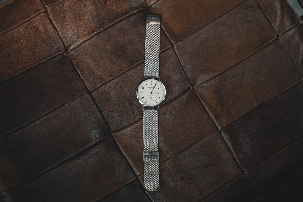 Silver watch with minimalist dial sitting on a brown leather piece of furniture