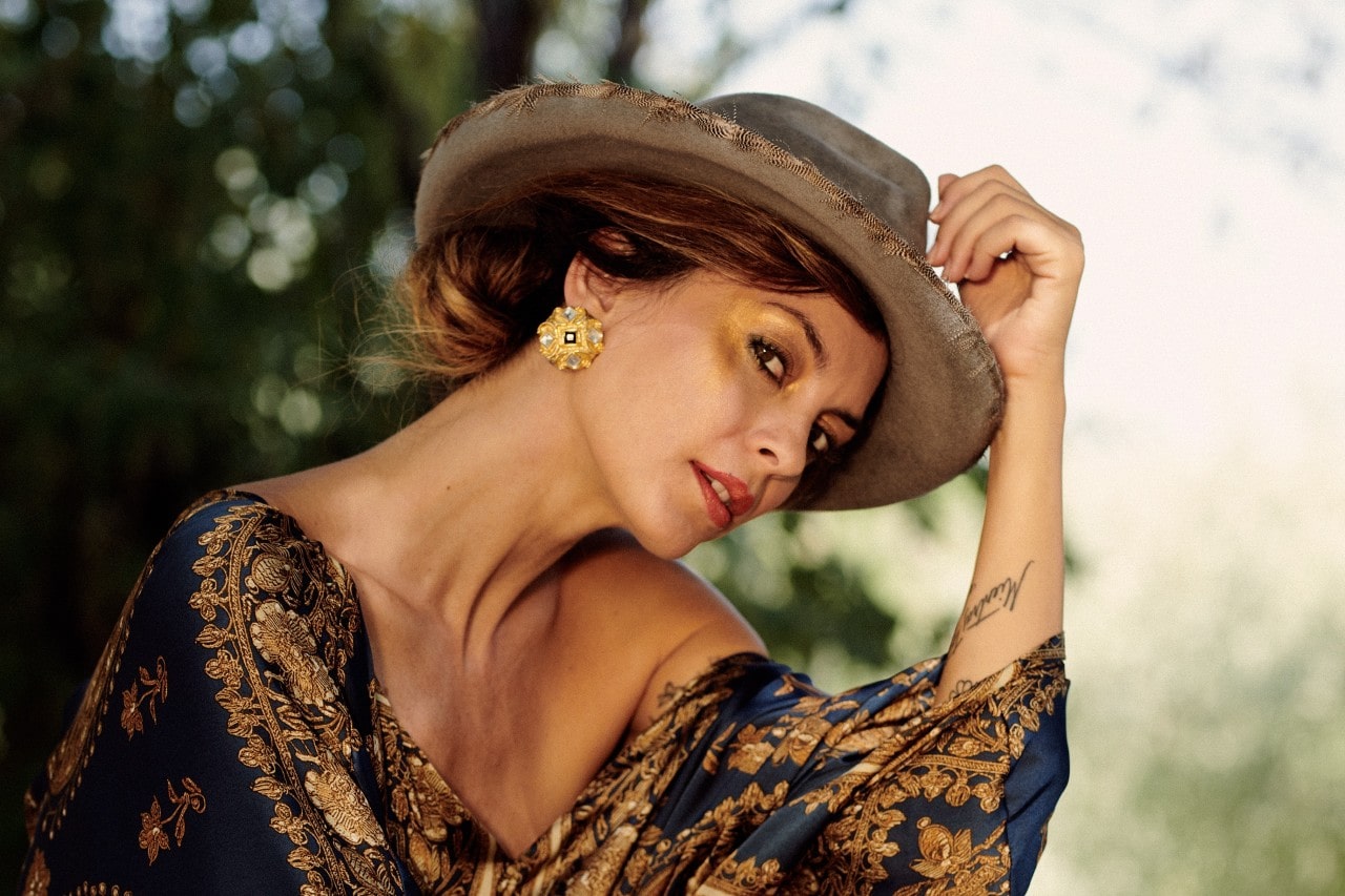 Woman in a fedora and bold, oversized stud earrings looking at the camera