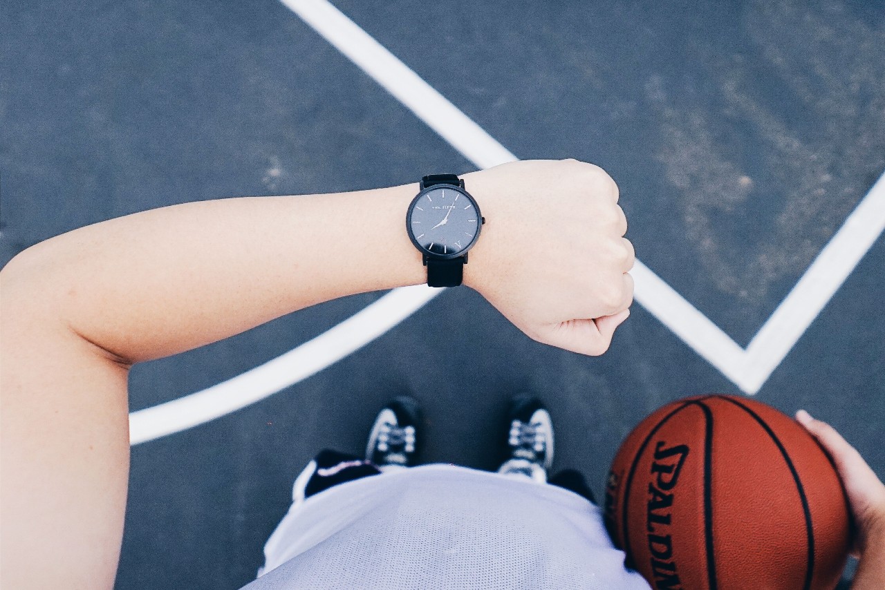 A person’s raised forearm wearing a black watch, holding a basketball in their other hand