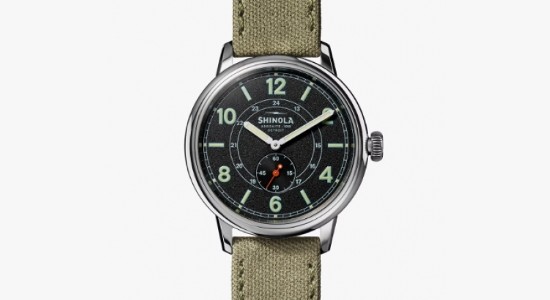 Silver Shinola watch with a textile strap, black dial face, and glow in the dark hands and indices