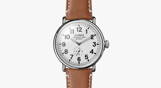A silver Shinola watch with a minimalist white watch dial and a brown leather strap
