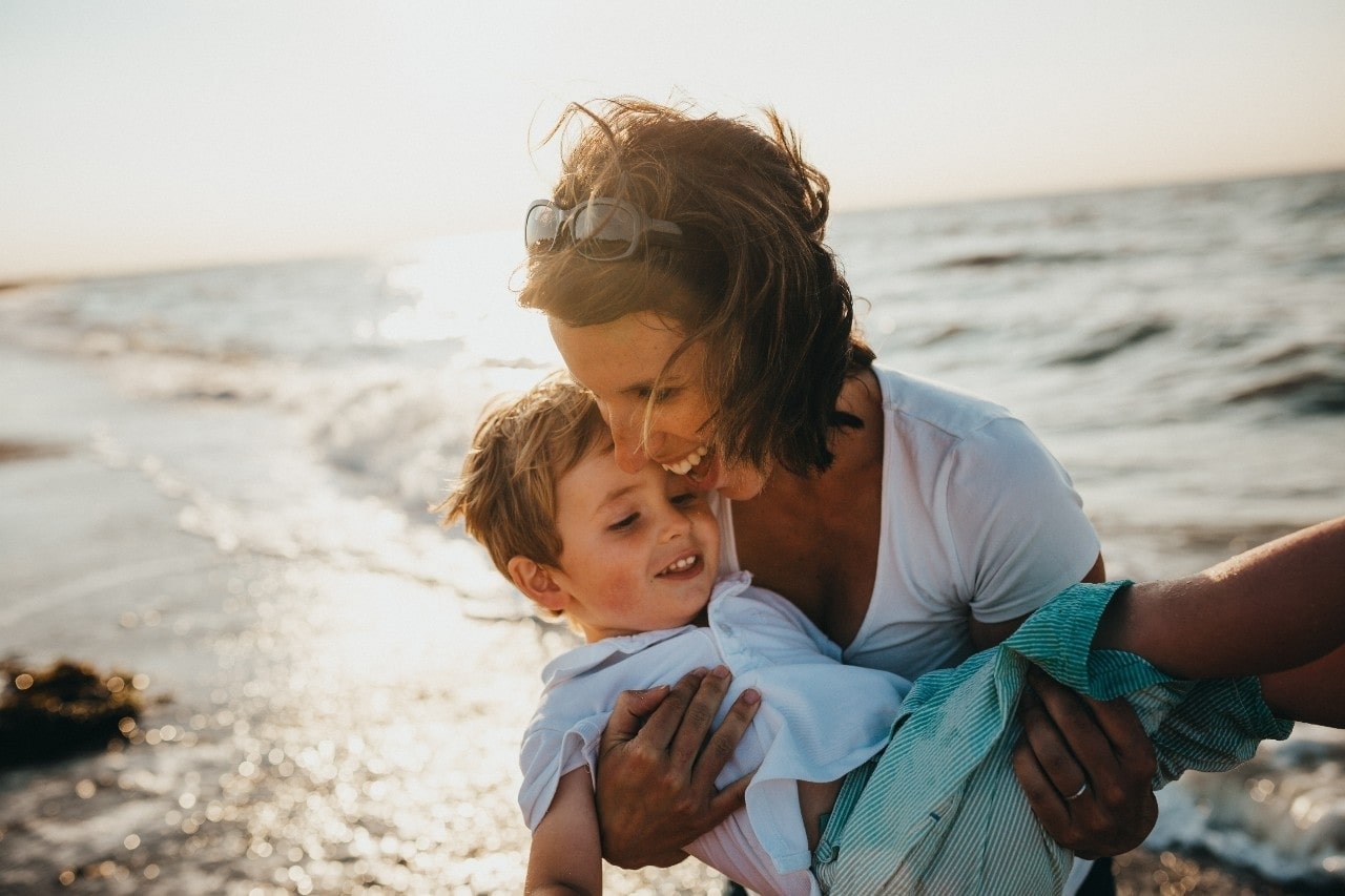 A woman carries her young son at the beach