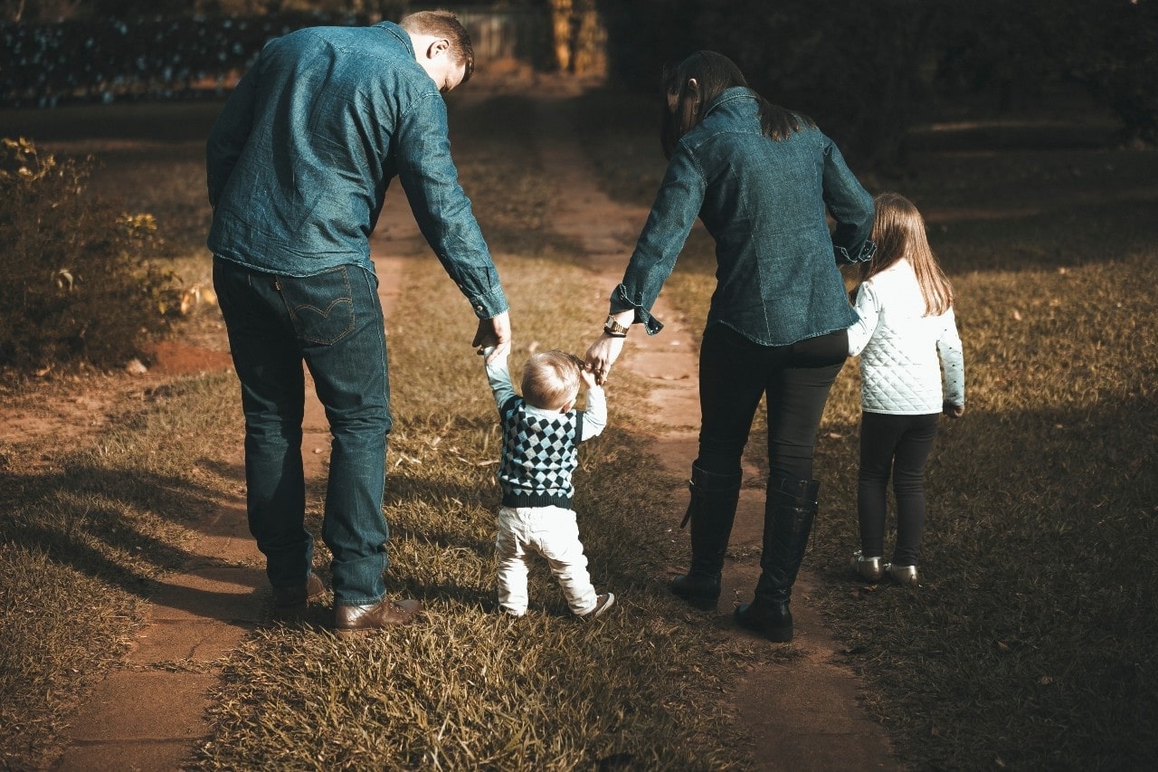 A young family holds hands and walks along a path