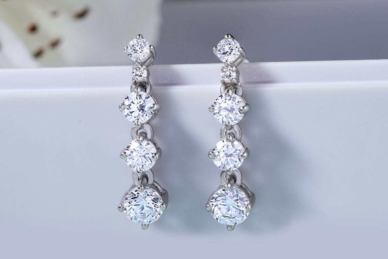 a pair of silver, tiered diamond earrings hanging on a white edge
