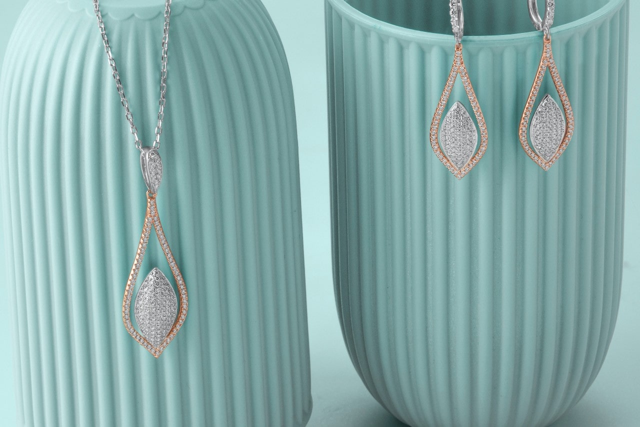 a matching set of mixed metal diamond earrings and a pendant necklace hanging on blue vases