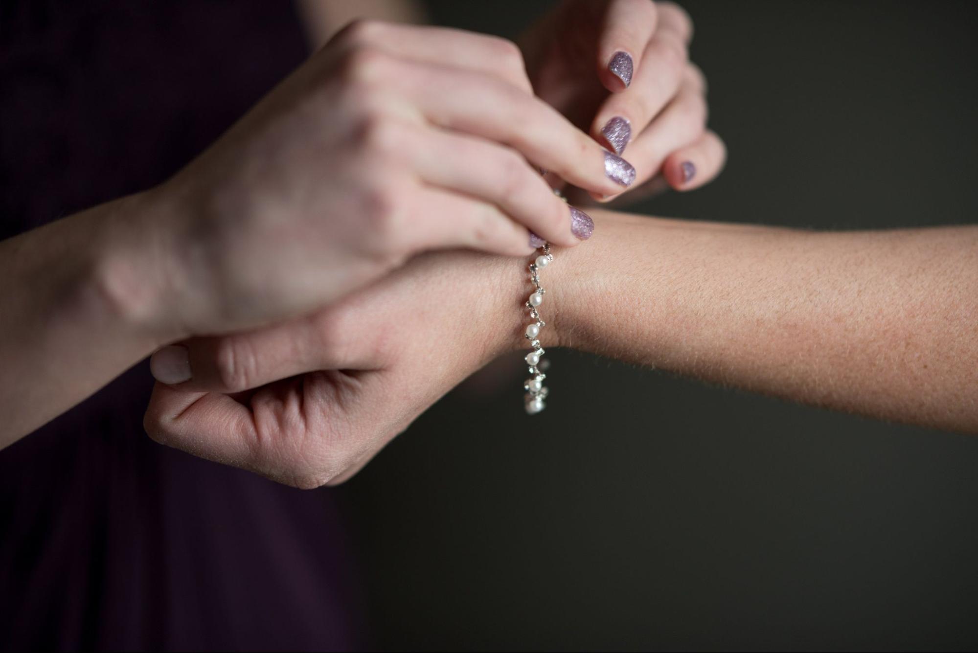 A pair of bridesmaids help each other put on their pearl bracelets.