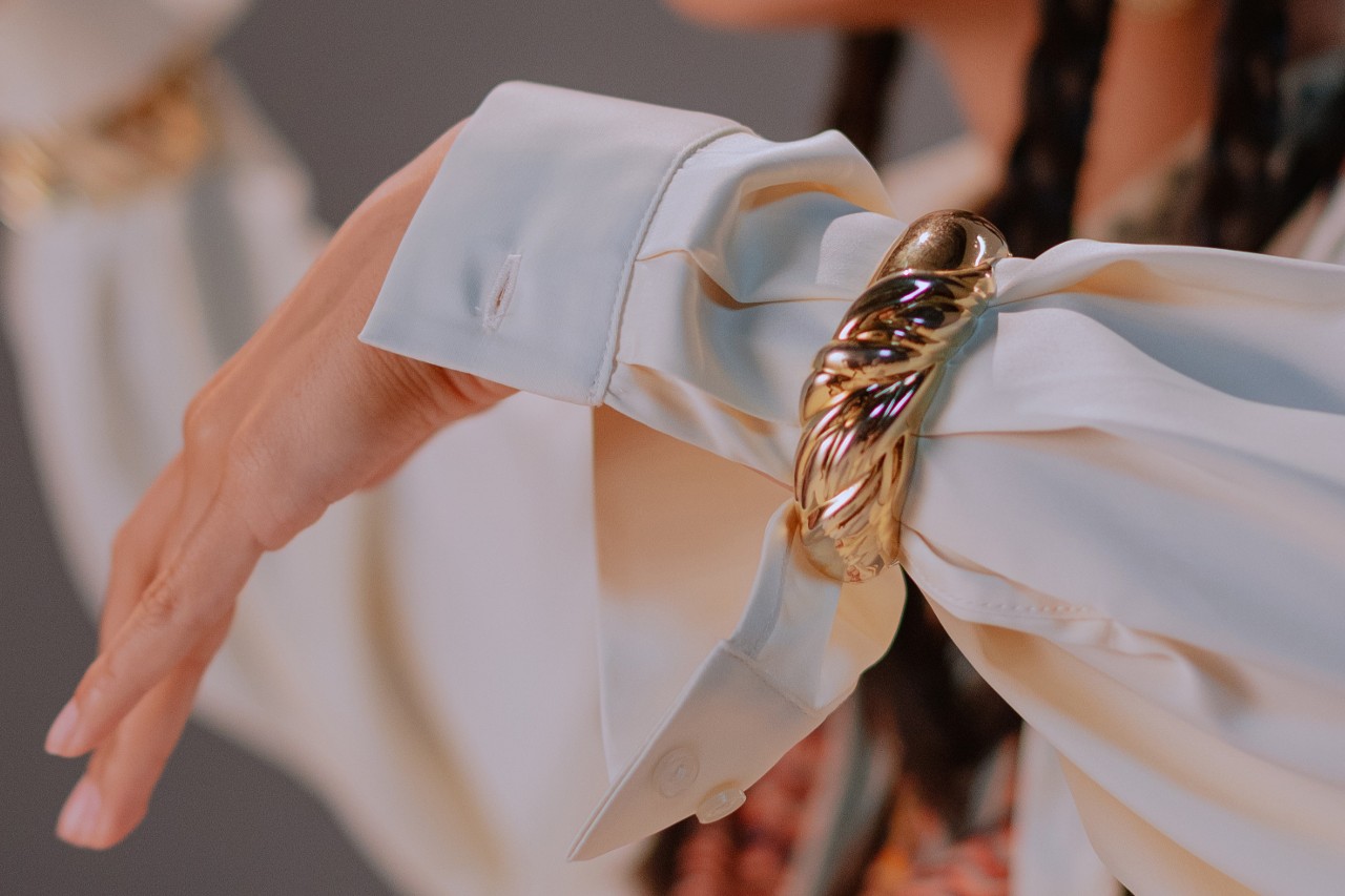 a woman’s arm donned in a white sleeve and a chunky gold bangle bracelet