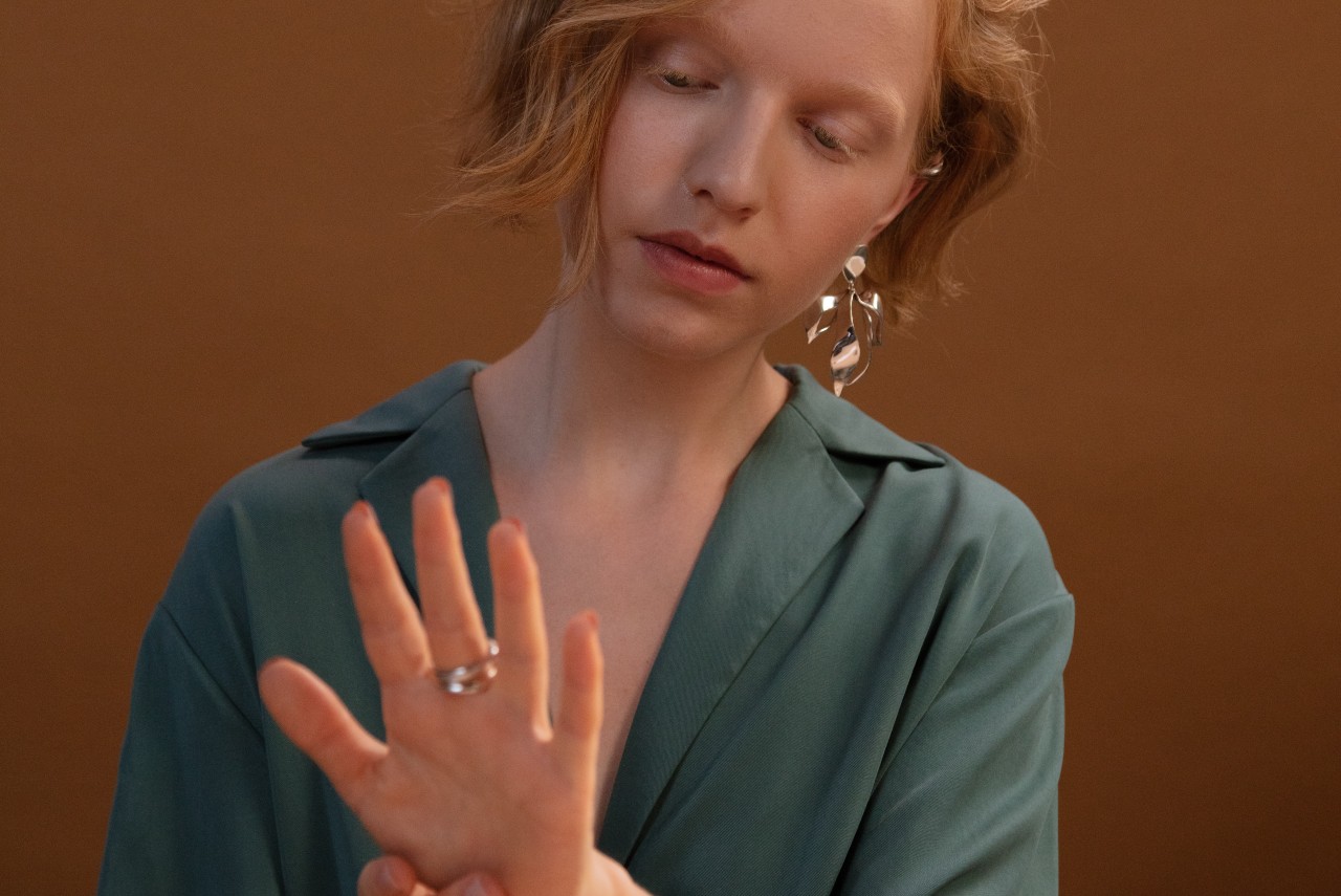 A redheaded woman in a green blouse inspects the white gold rings she is wearing.