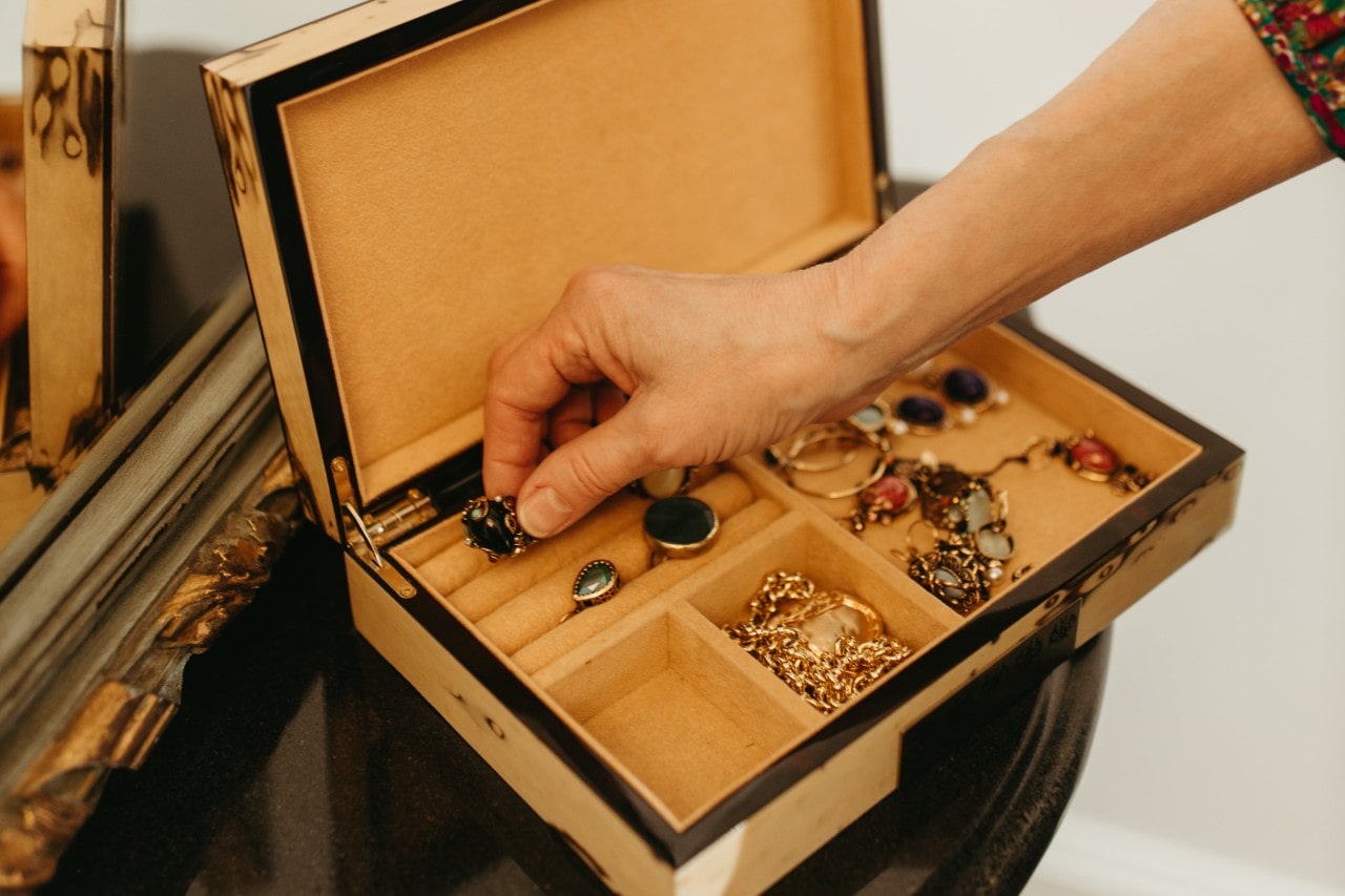 a person’s hand selecting a gemstone ring out of a jewelry box