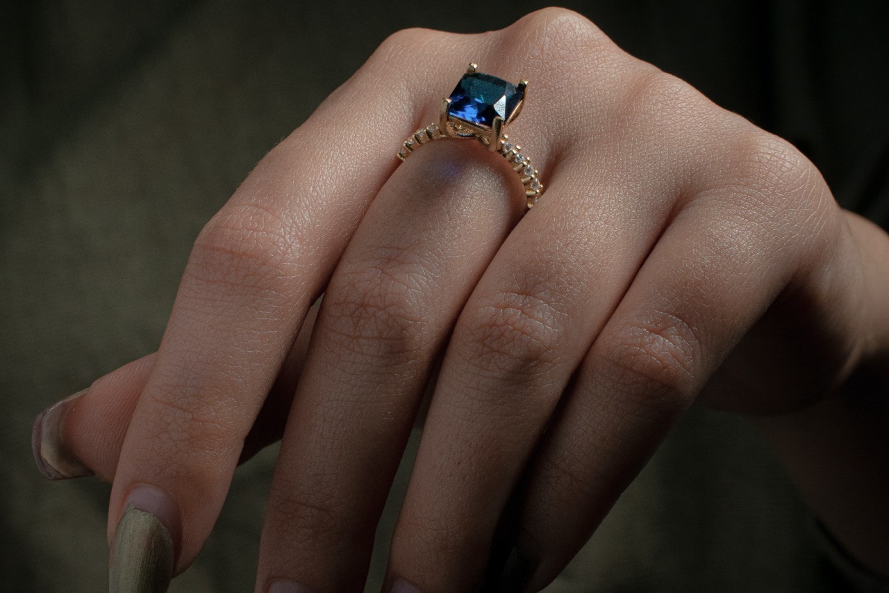 close up image of a hand adorned with a princess cut sapphire ring