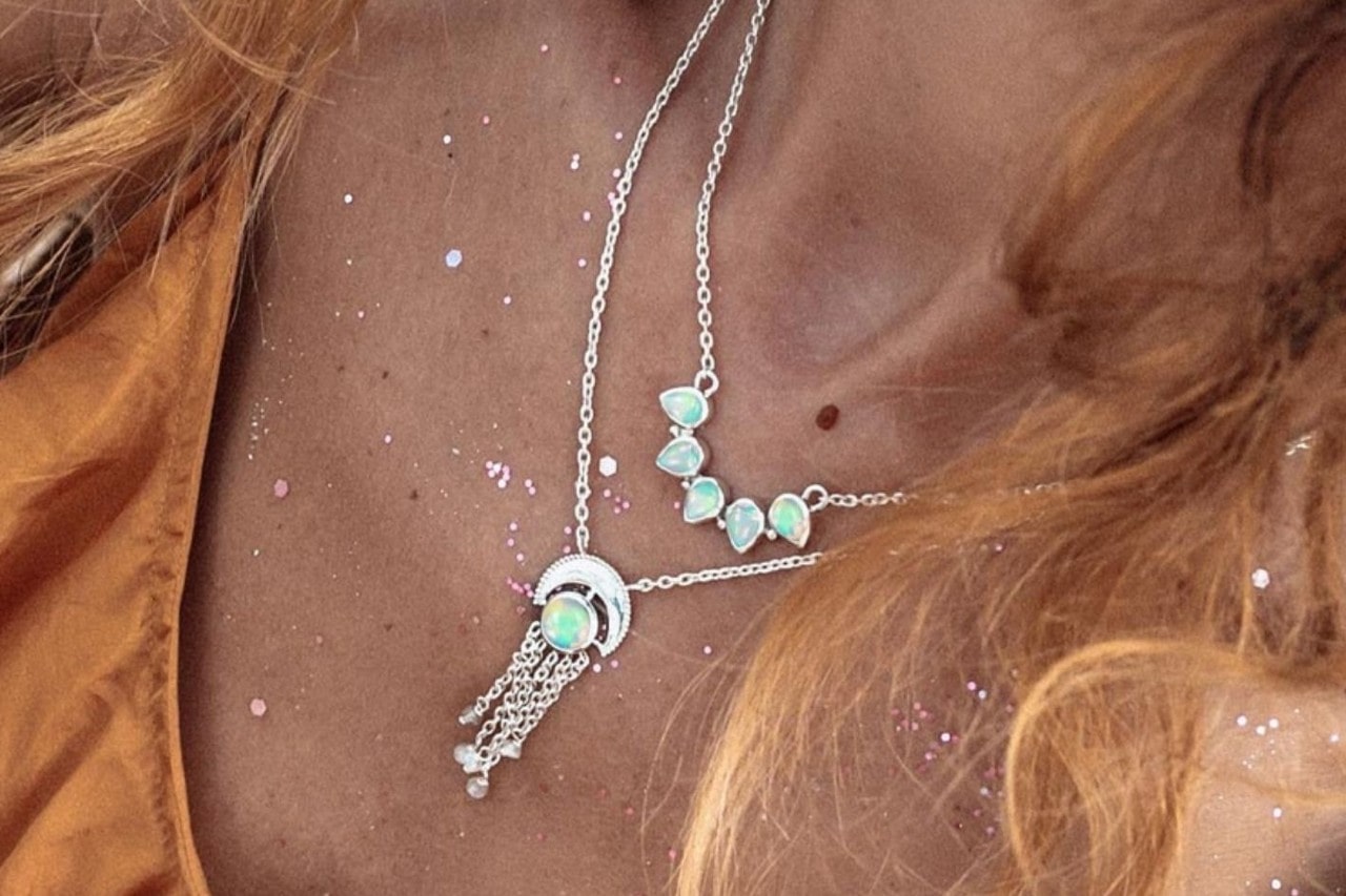 close up image of a woman wearing two silver necklaces featuring colorful opals