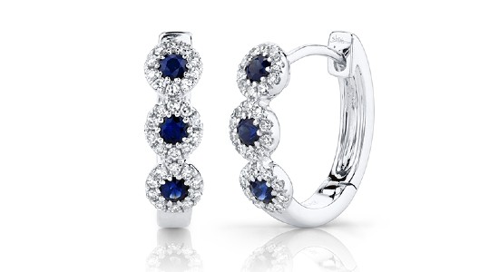 a pair of silver huggie earrings each with three sapphires surrounded by accent diamonds