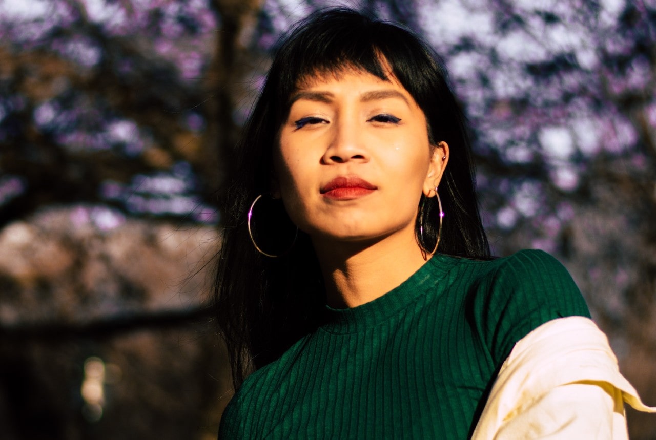 a woman wearing a pair of hoop earrings with a green blouse and white jacket.