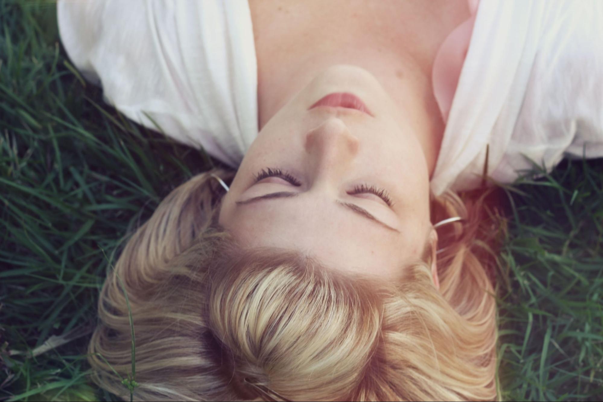 A woman lays down on grass, wearing a pair of yellow gold hoop earrings.