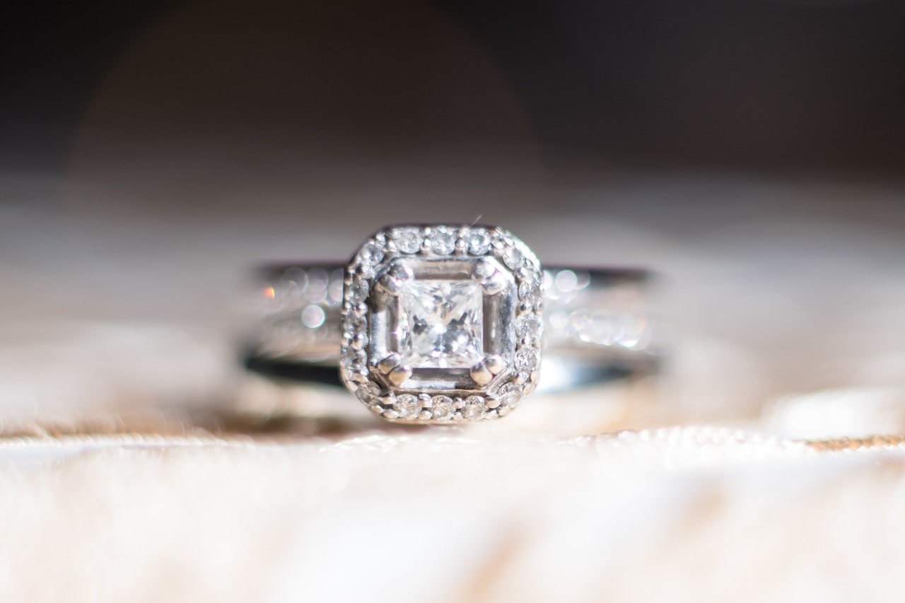 A cushion-cut diamond halo engagement ring sits on a cream-colored satin surface.
