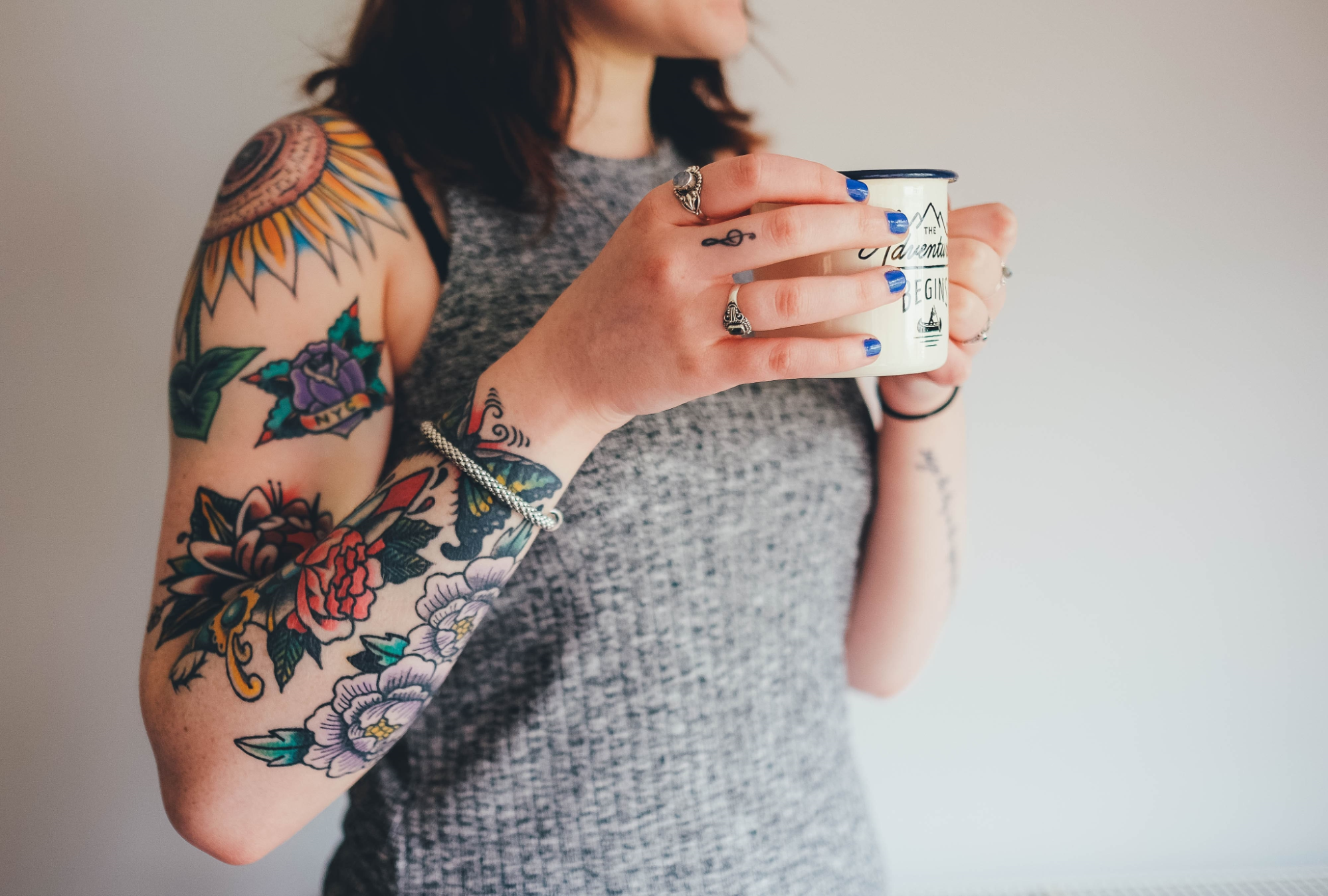 lady with tattoos on her arms holding a coffee mug and wearing bracelets