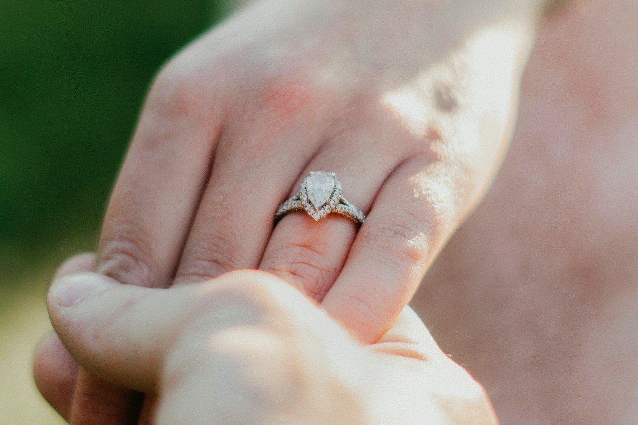 close up image of a person’s hand wearing a white gold engagement ring with a pear shaped center stone