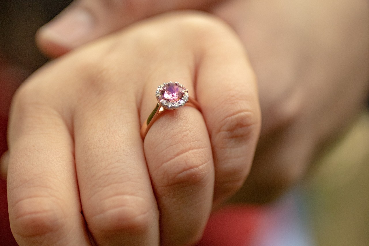 close up image of a person’s hand wearing a rose gold engagement ring with a purple center stone