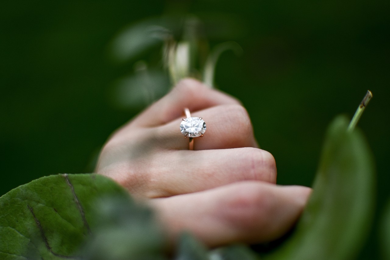 close up image of a hand holding the stems of a bouquet and wearing a solitaire engagement ring