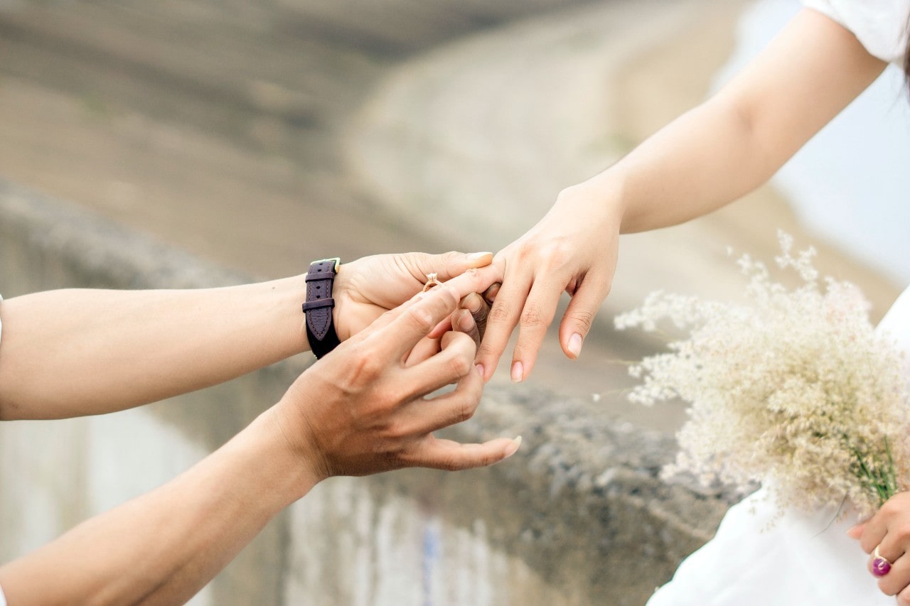 a person placing an engagement ring on the finger of a woman holding flowers