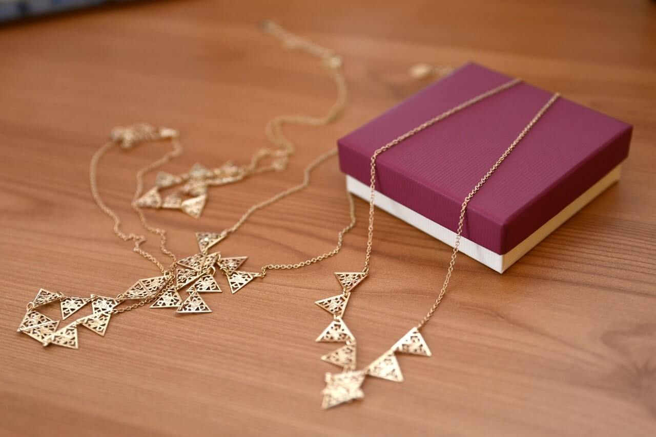A yellow gold geometric-design necklace sits on a wooden table outside of its original box