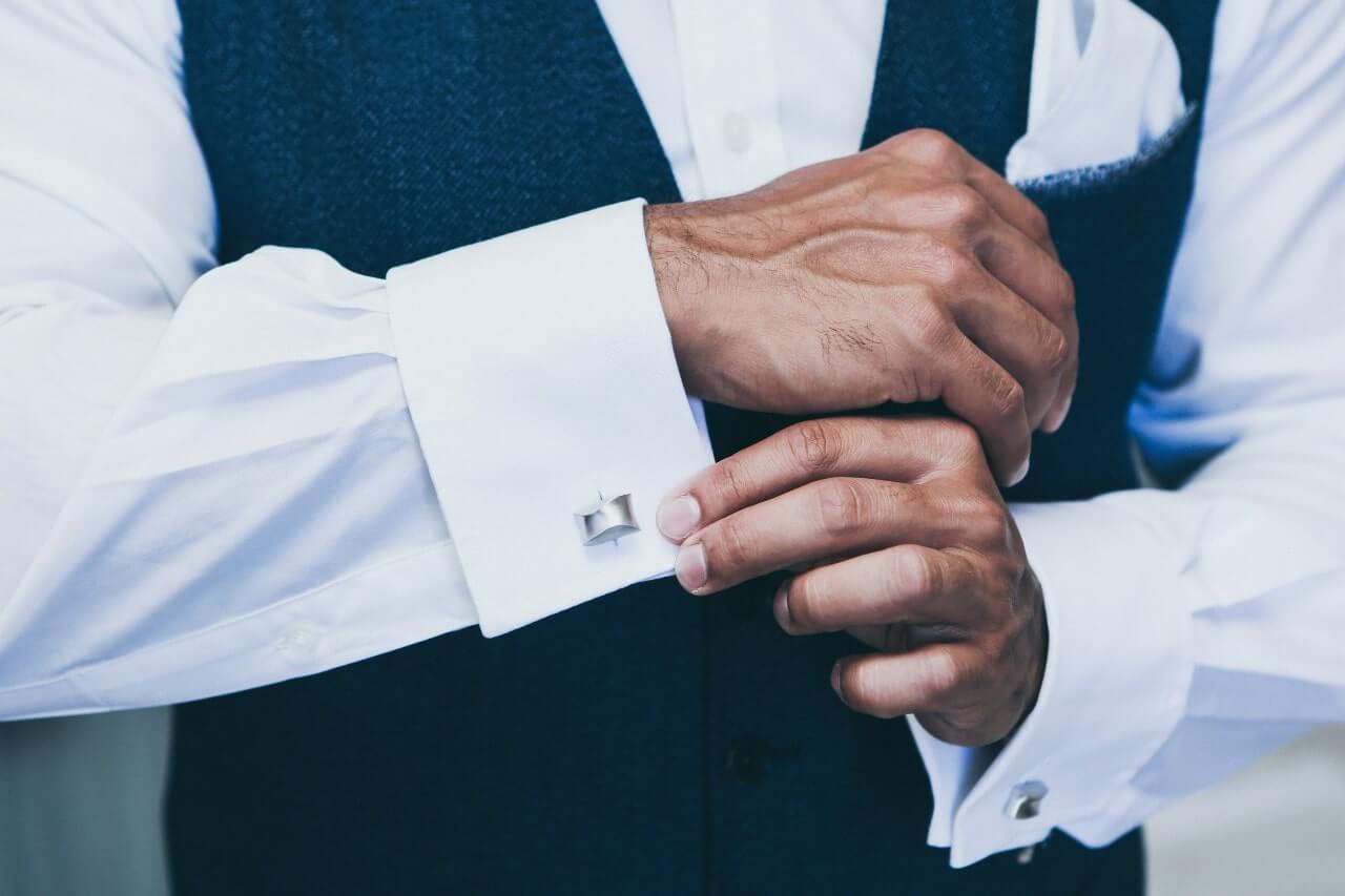 A man adjusts his white gold cufflinks while getting dressed for a business day