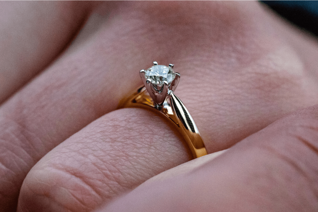 A gold solitaire engagement ring with a round cut diamond on a ring finger.