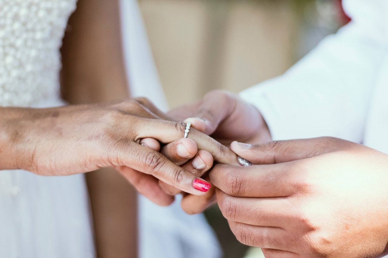 A groom slips a half eternity diamond wedding band on his bride’s ring finger.